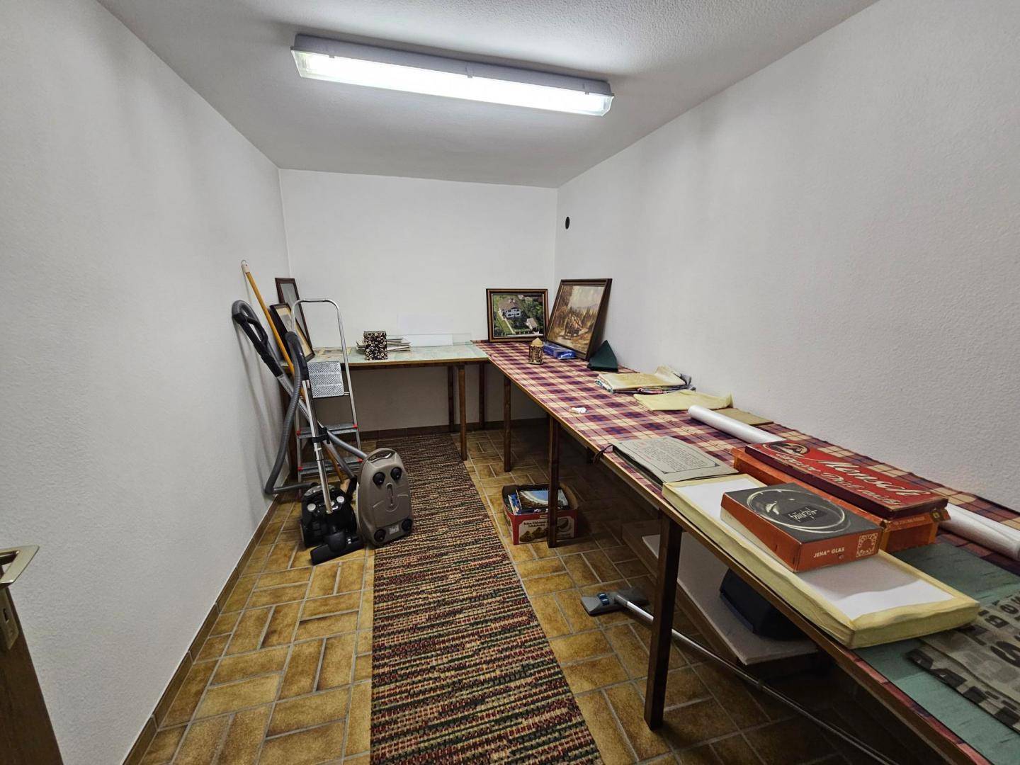 Funktionaler Abstellraum im Keller mit gefliestem Boden und einfacher Beleuchtung.