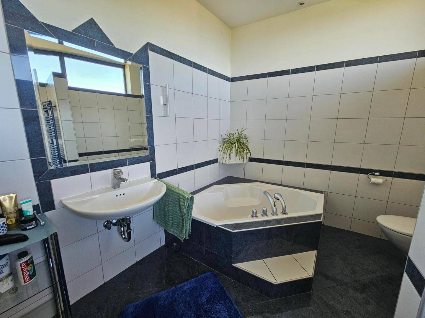 Badezimmer mit Eckbadewanne, Waschbecken und Fliesen in Weiß und Dunkelblau.
