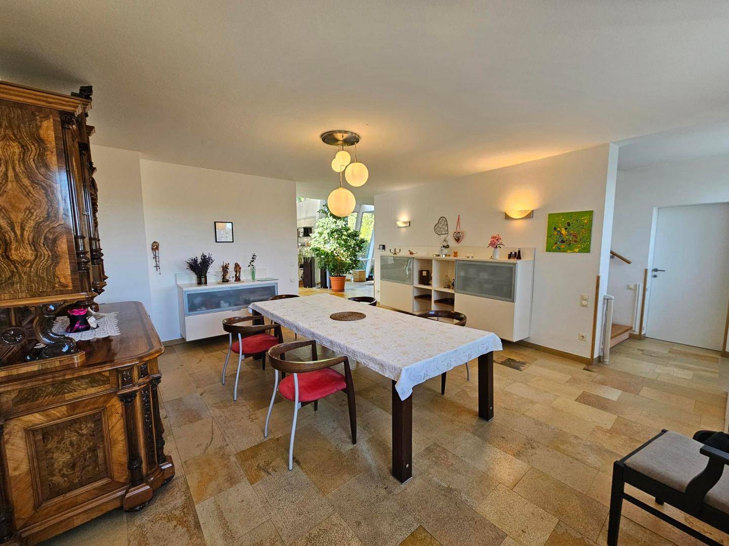 Essbereich mit großem Holztisch, modernen Leuchten und traditionellen Möbelstücken auf Steinboden.