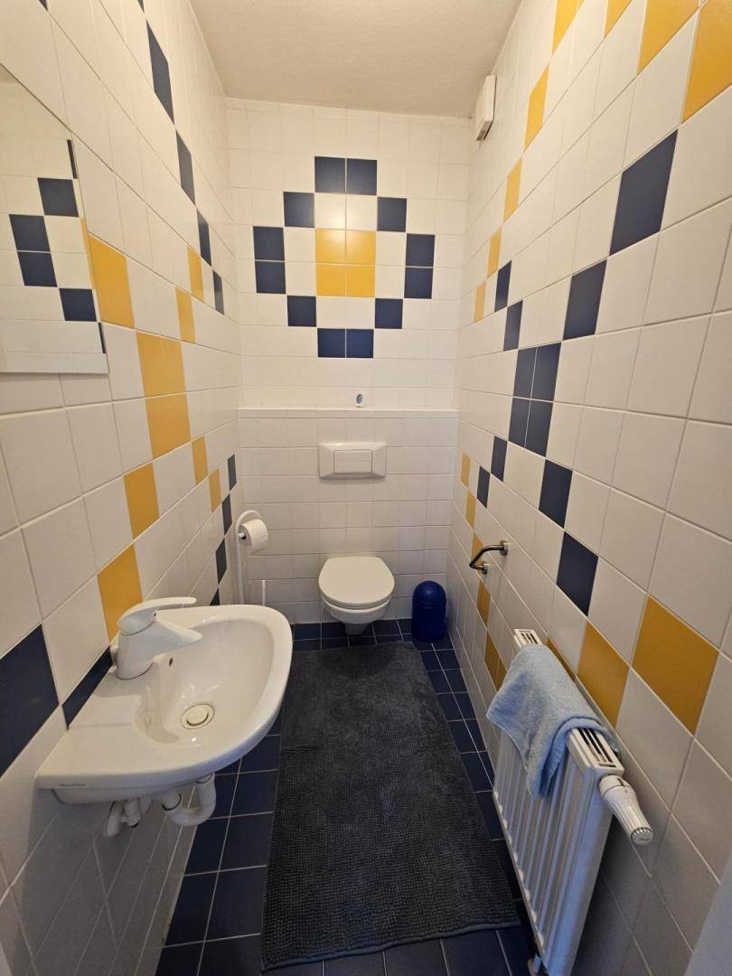 Gäste-WC mit farbenfrohen Fliesen in Gelb und Blau, Waschbecken und Wand-WC.