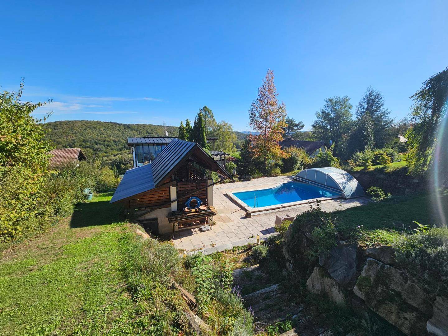 Außenbereich mit Pool, Sonnenterrasse und einer rustikalen Holzlaube im Grünen.