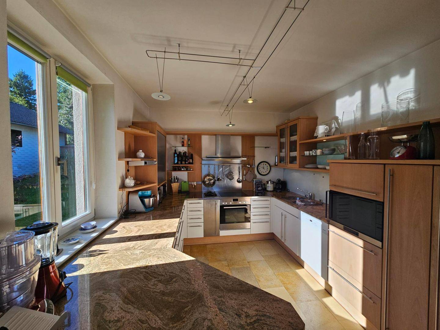 Geräumige Küche mit Holzschränken, Granitarbeitsplatten und viel Tageslicht durch große Fenster.