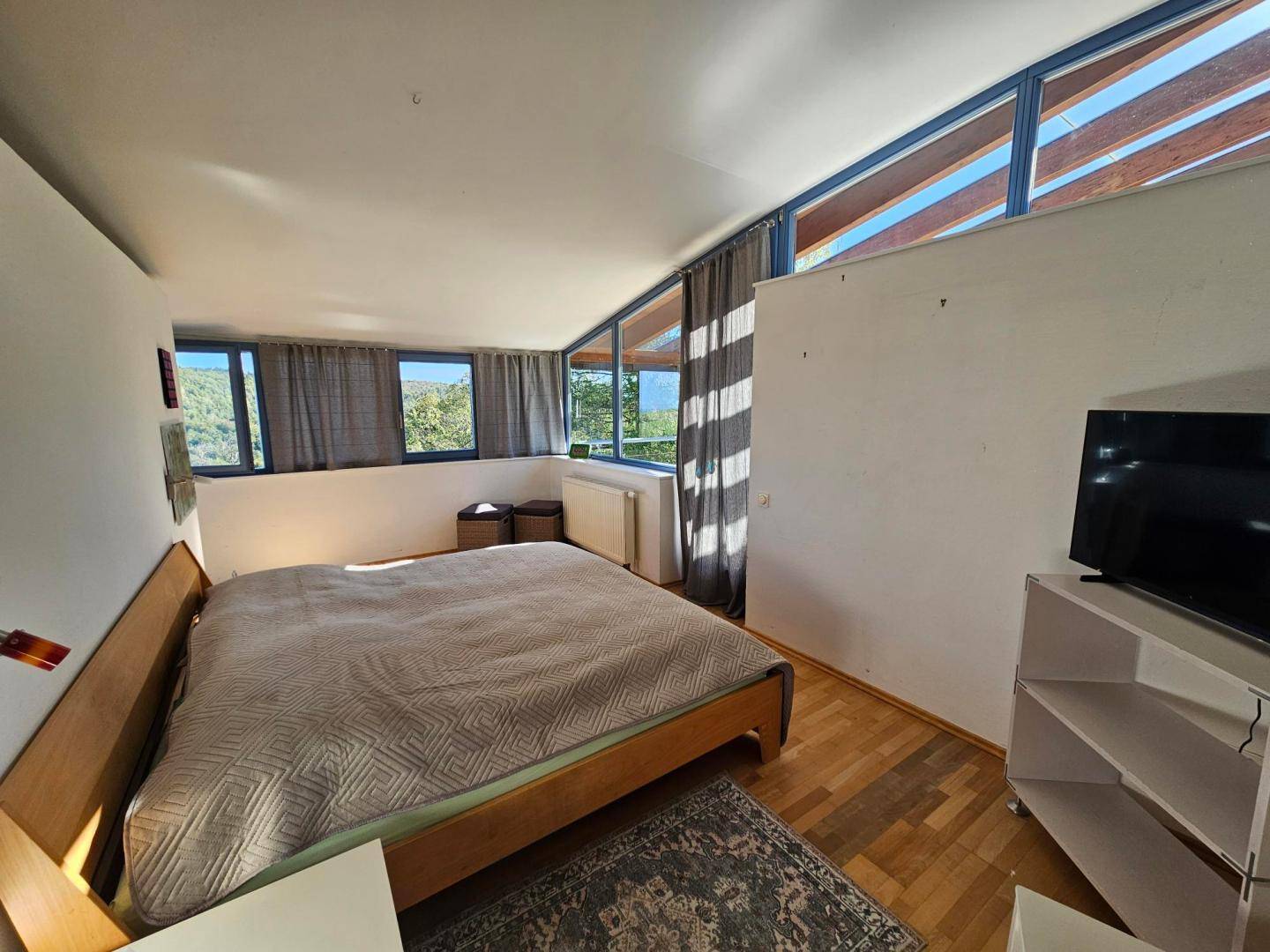 Schlafzimmer mit Holzboden, großen Fenstern und Blick auf die umliegende Landschaft.