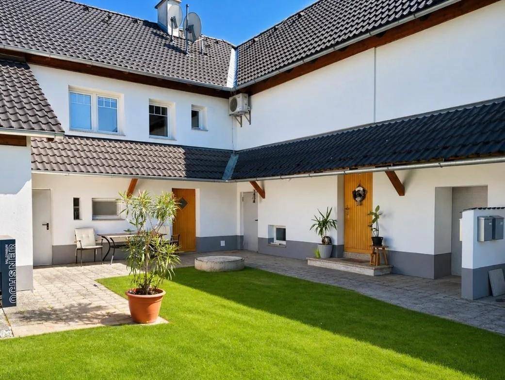 Heller Innenhof mit gepflegtem Rasen, gepflastertem Bereich und Pflanzen in Töpfen.