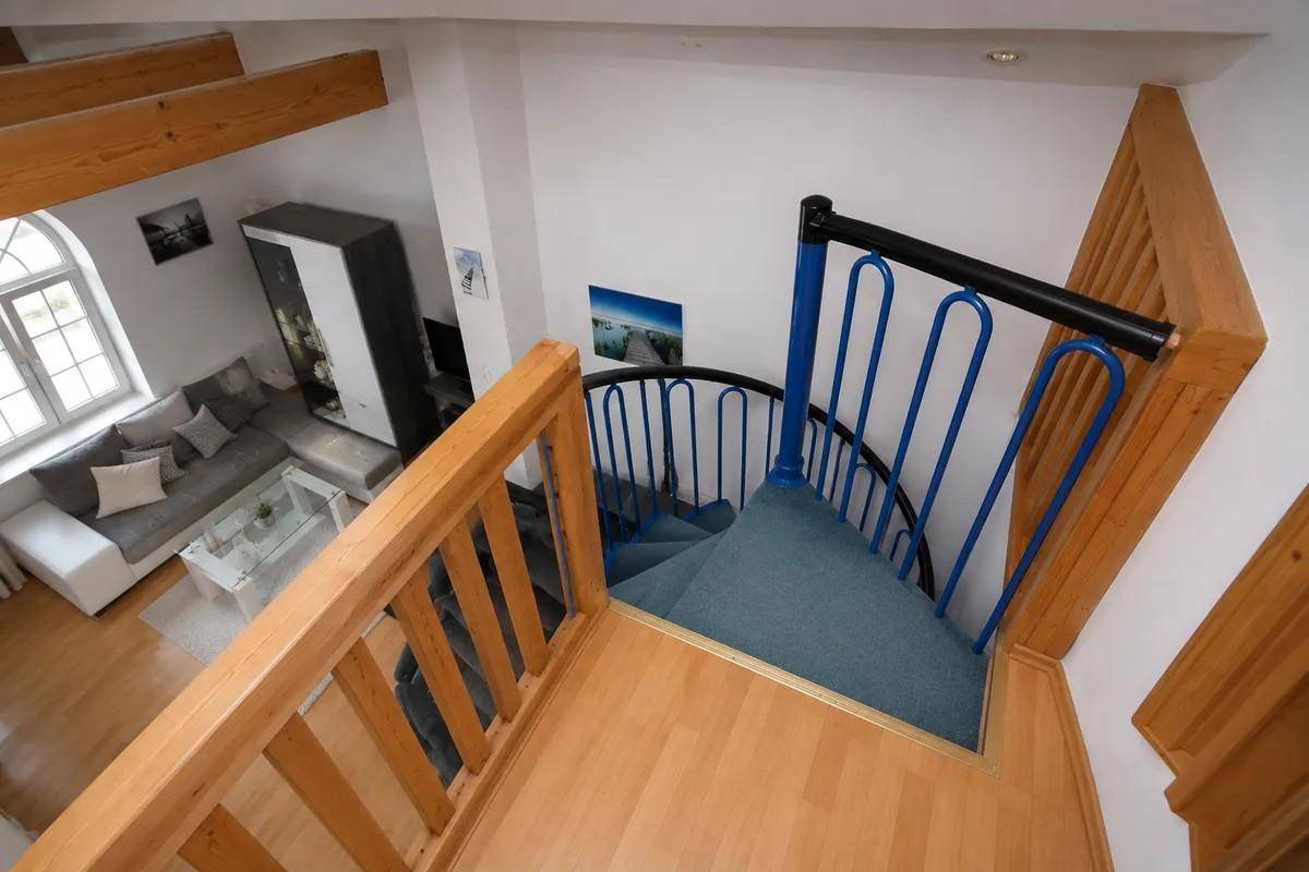 Wendeltreppe mit blauem Geländer, die zu einem hellen Wohnbereich mit Holzboden führt.