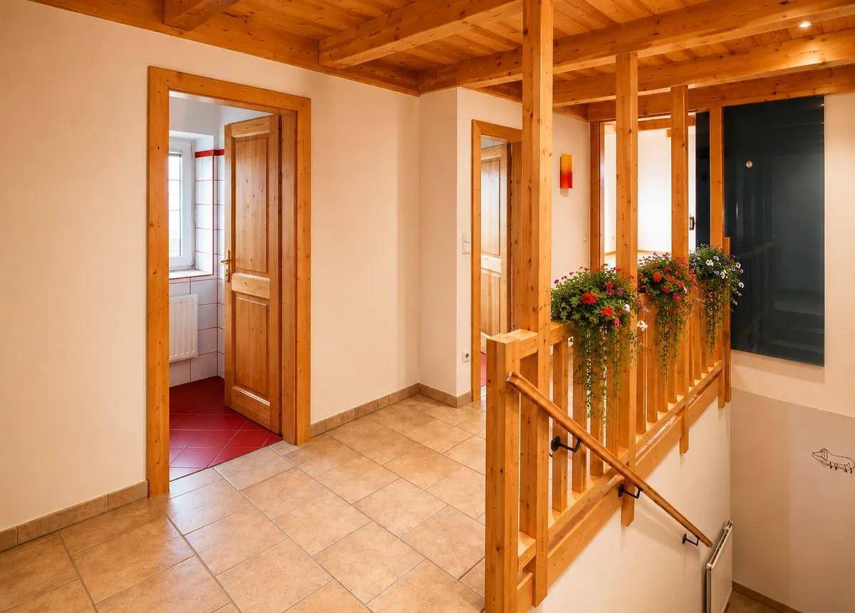 Heller Flur mit Holzgeländer, Holzbalken und gefliestem Boden, der zu weiteren Räumen führt.