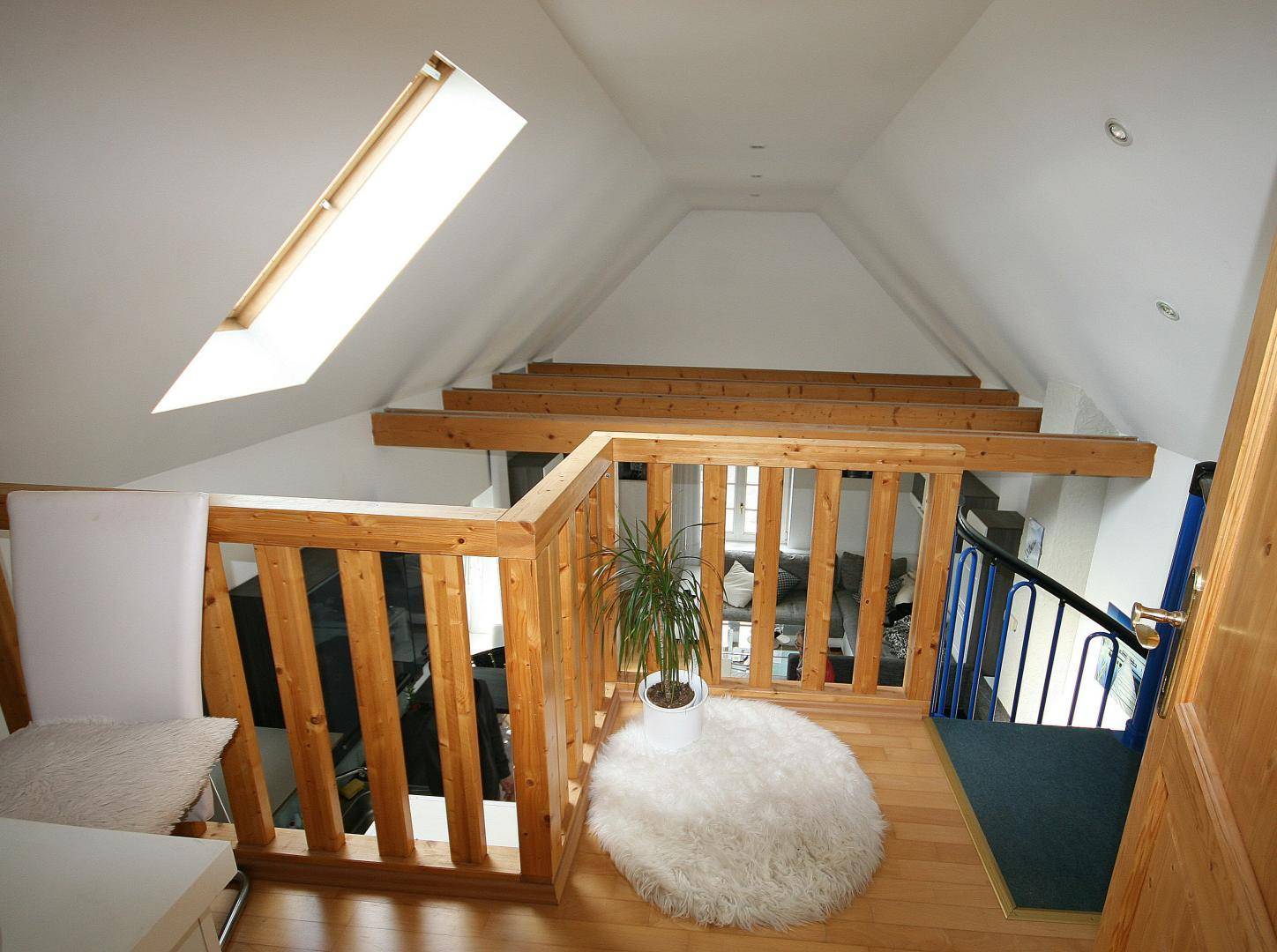 Heller Loftbereich mit Holzgeländer, Dachfenster und Blick auf den darunterliegenden Wohnraum.