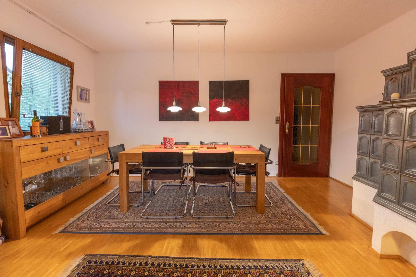 Heller Essbereich mit Holztisch, Parkettboden und traditionellem Kachelofen.