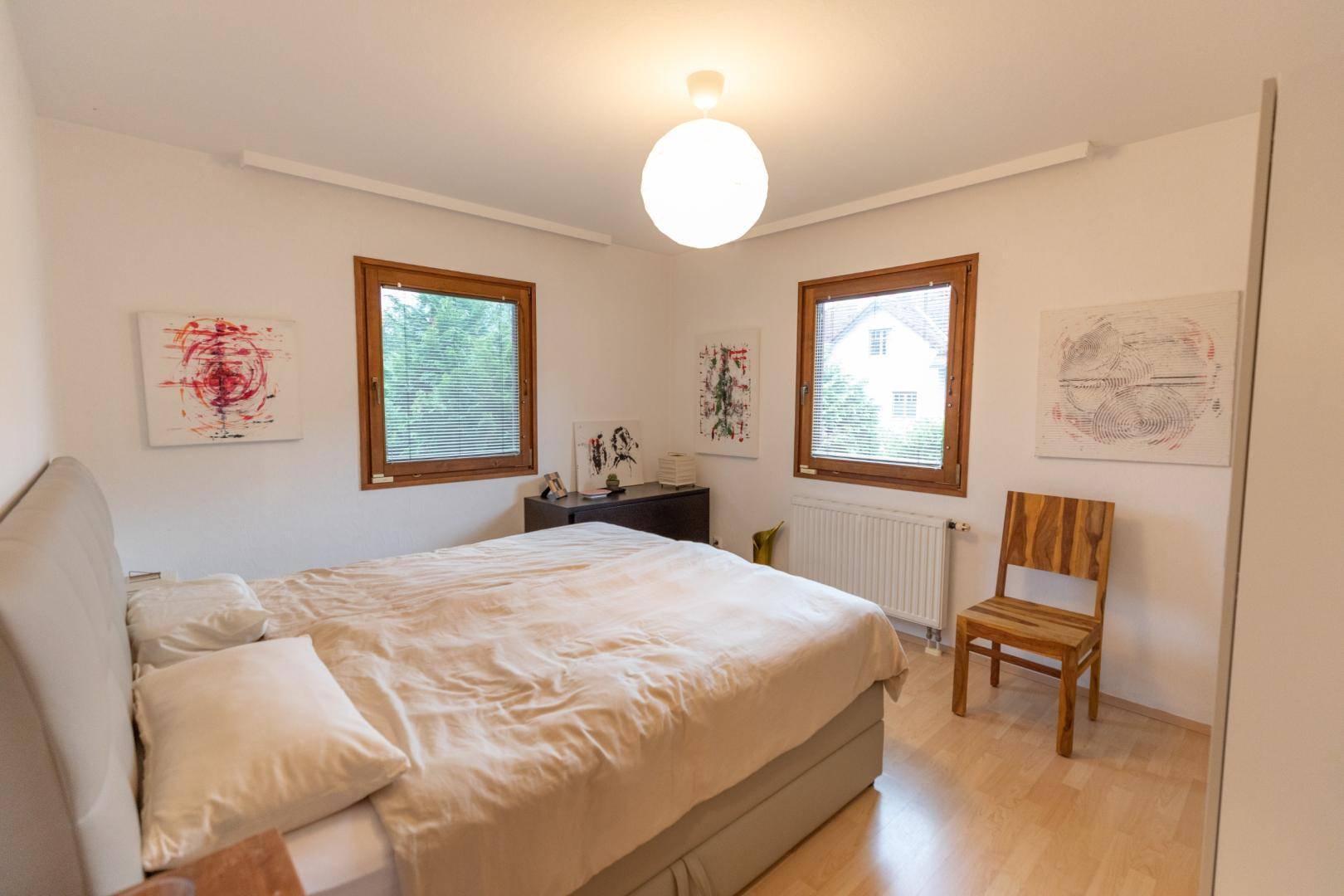Schlafzimmer mit Doppelbett, Holzboden und zwei Fenstern für natürliches Licht.
