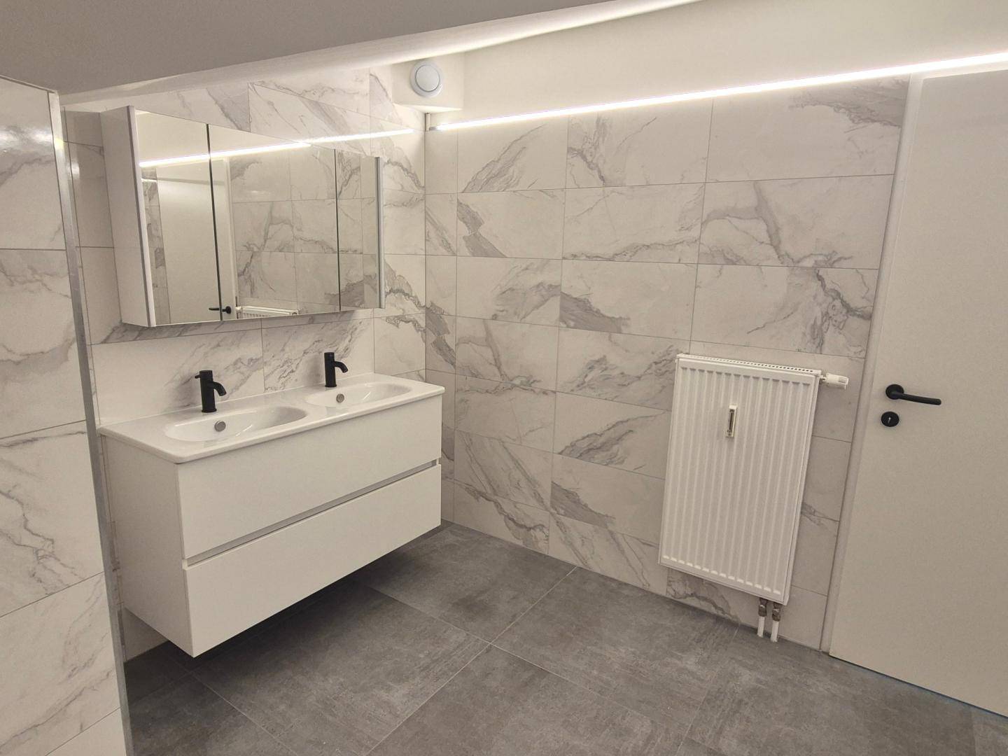 Geräumiges Badezimmer mit Doppelwaschbecken, Spiegelschrank und modernen Fliesen in Marmoroptik.