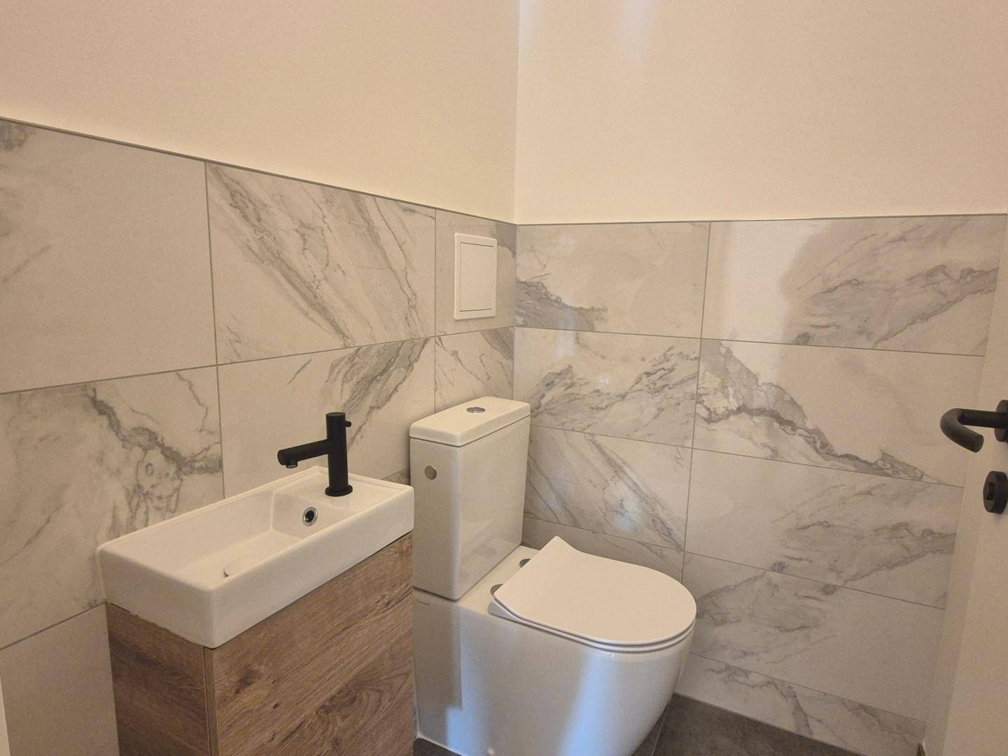 Stilvolles Gäste-WC mit wandhängender Toilette, kleinem Waschbecken und Marmoroptik-Fliesen.