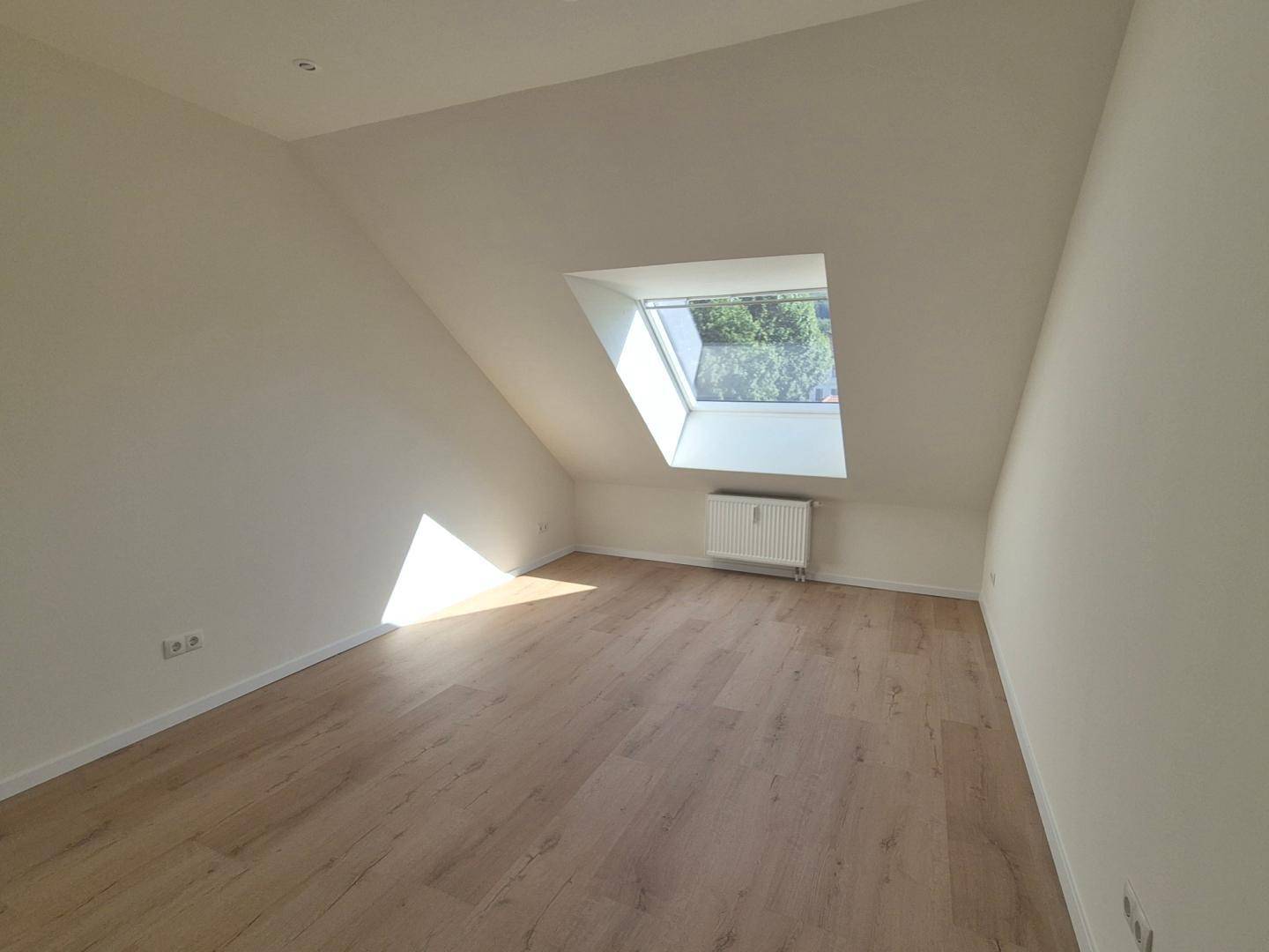 Lichtdurchfluteter Dachgeschossraum mit großem Dachfenster und hellem Laminatboden.