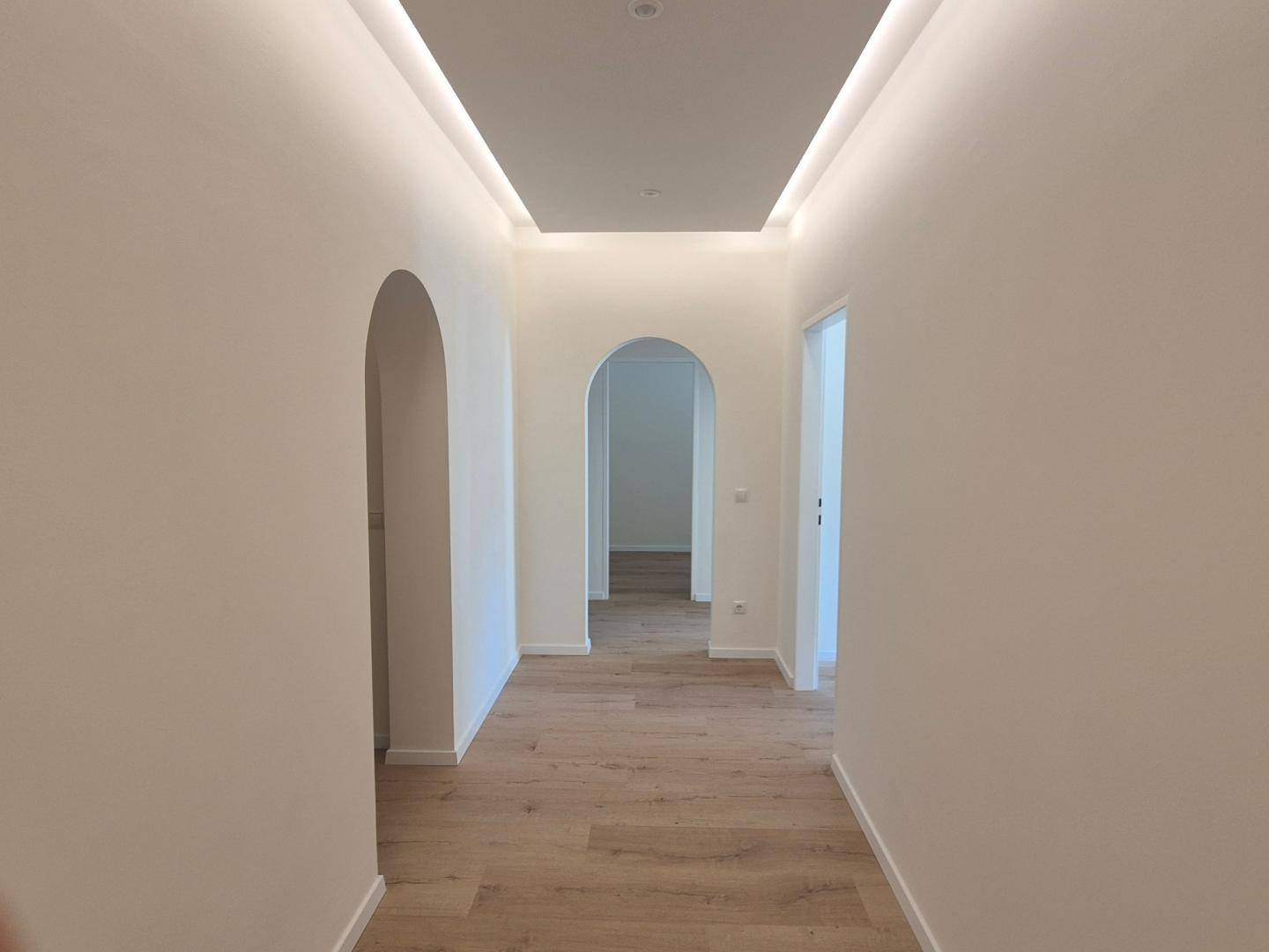 Langer Flur mit eleganten Rundbögen, modernem Laminatboden und indirekter Deckenbeleuchtung.