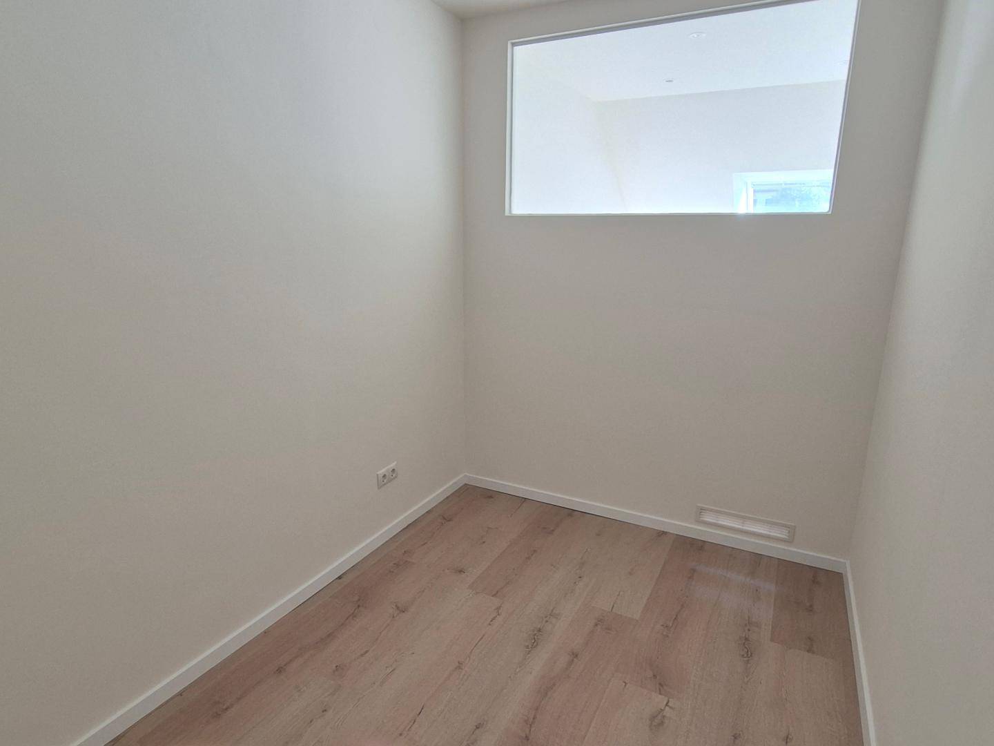 Kleiner, heller Raum mit hohem Fenster und modernem Laminatboden, ideal als Abstellraum.
