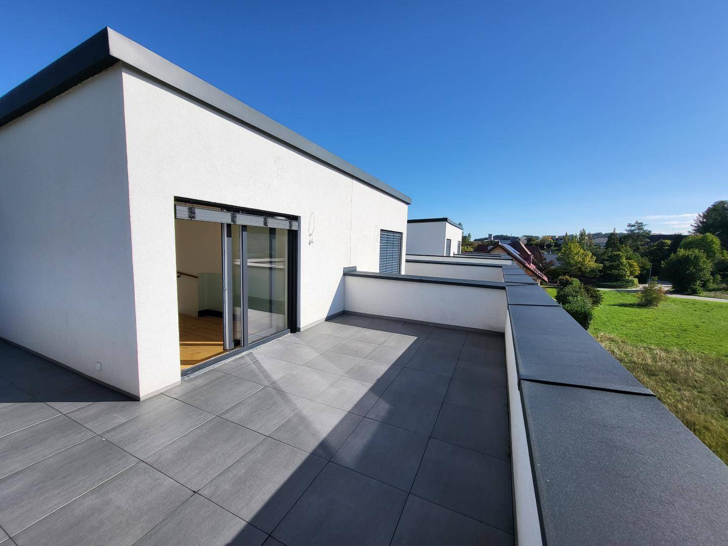 Geräumige Dachterrasse mit modernen Fliesen und weitem Blick ins Grüne.