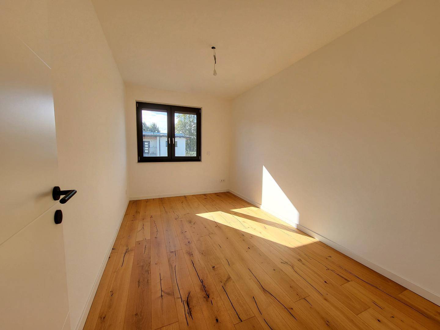Helles, unmöbliertes Schlafzimmer mit Holzboden und Fenster.
