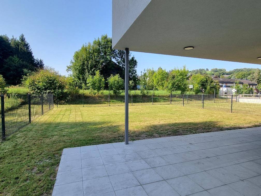 Große geflieste Terrasse mit weitem Blick auf den gepflegten Rasen und die grüne, bewaldete Umgebung.