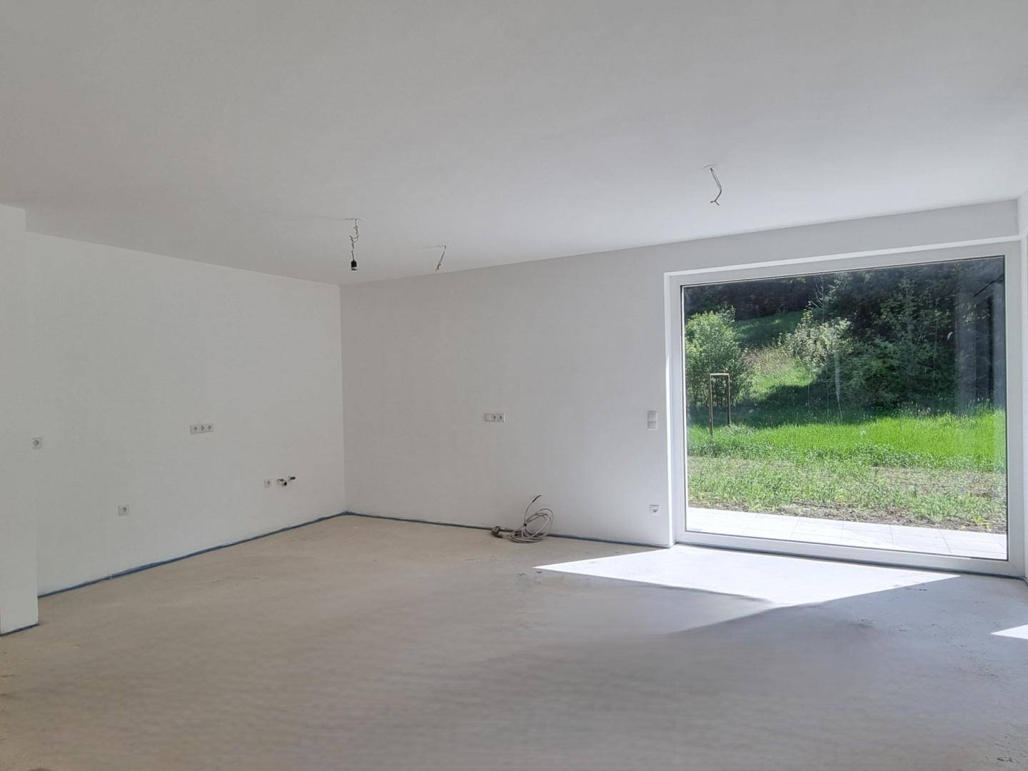 Heller Wohnraum im Rohbau mit großer Fensterfront und Zugang zur Terrasse.
