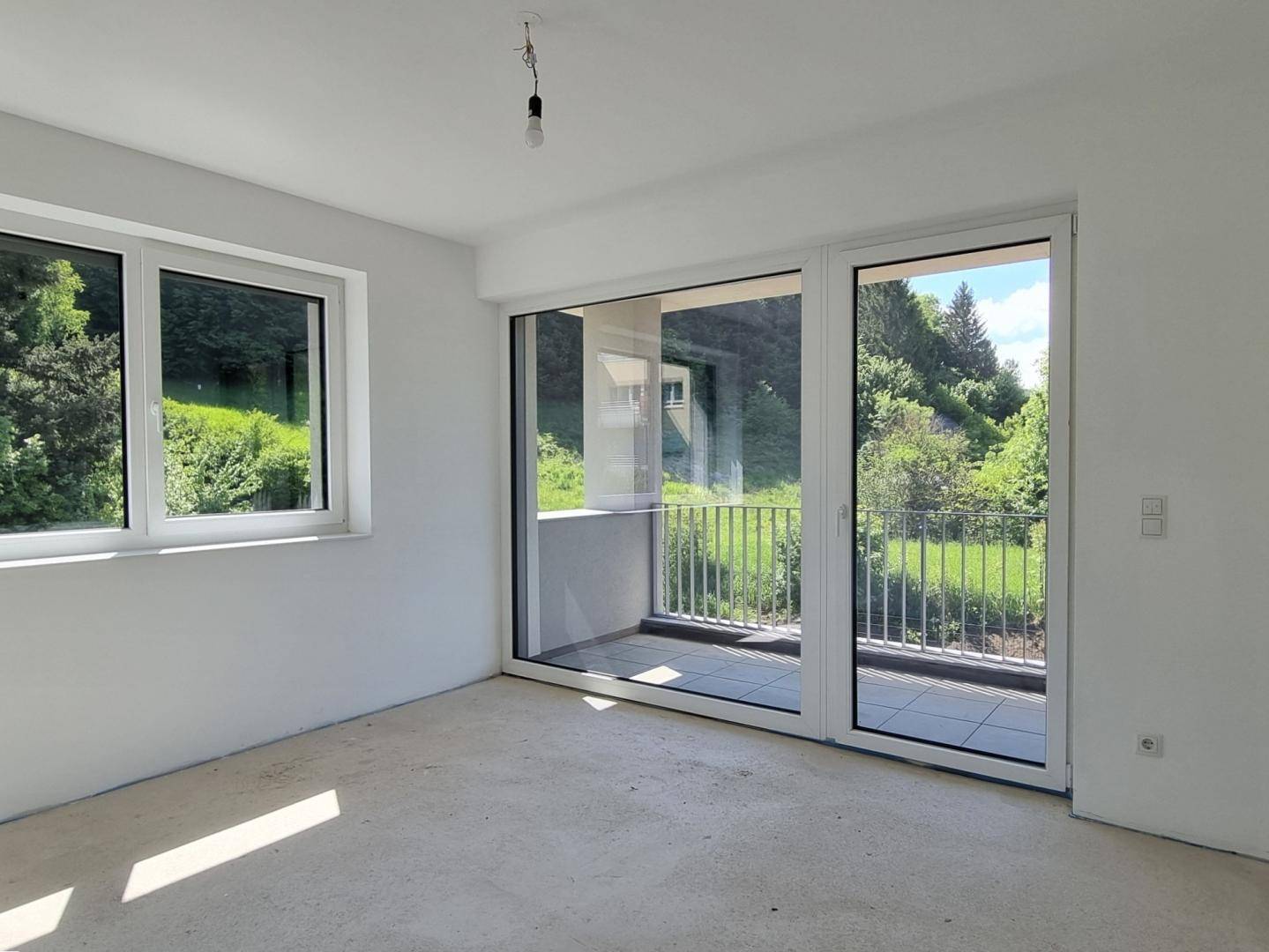 Schlafzimmer im Rohbau mit Fenster und Zugang zum Balkon mit Blick ins Grüne.