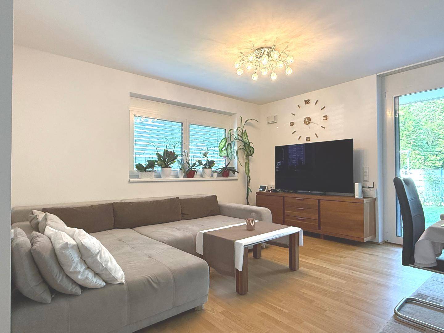 Geräumiges Wohnzimmer mit beigem Ecksofa, Holzboden und großen Fenstern für viel Tageslicht.