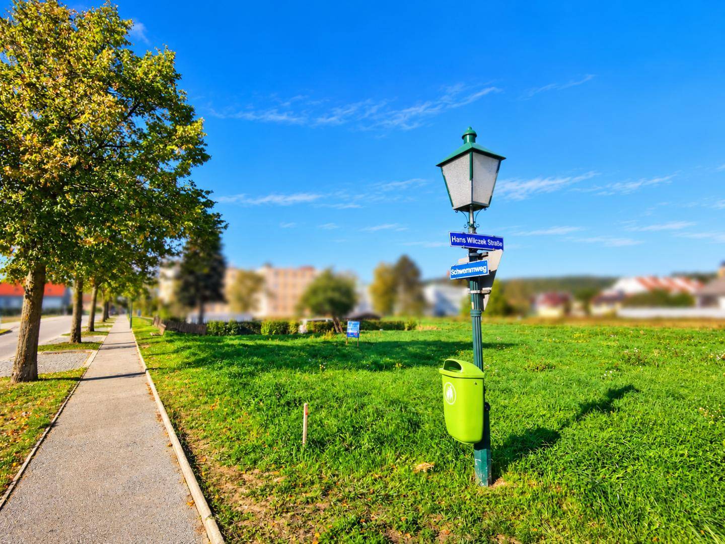 Grünes Grundstück mit Gehweg, Straßenlaterne und Bäumen unter klarem blauem Himmel.