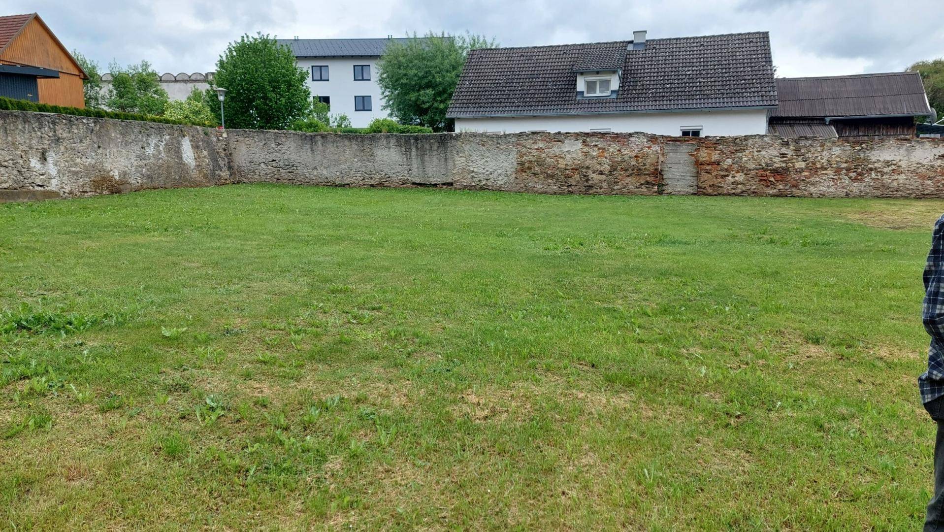 Weitläufige, gepflegte Rasenfläche, begrenzt von einer historischen Steinmauer, ideal für Erholung im Freien.