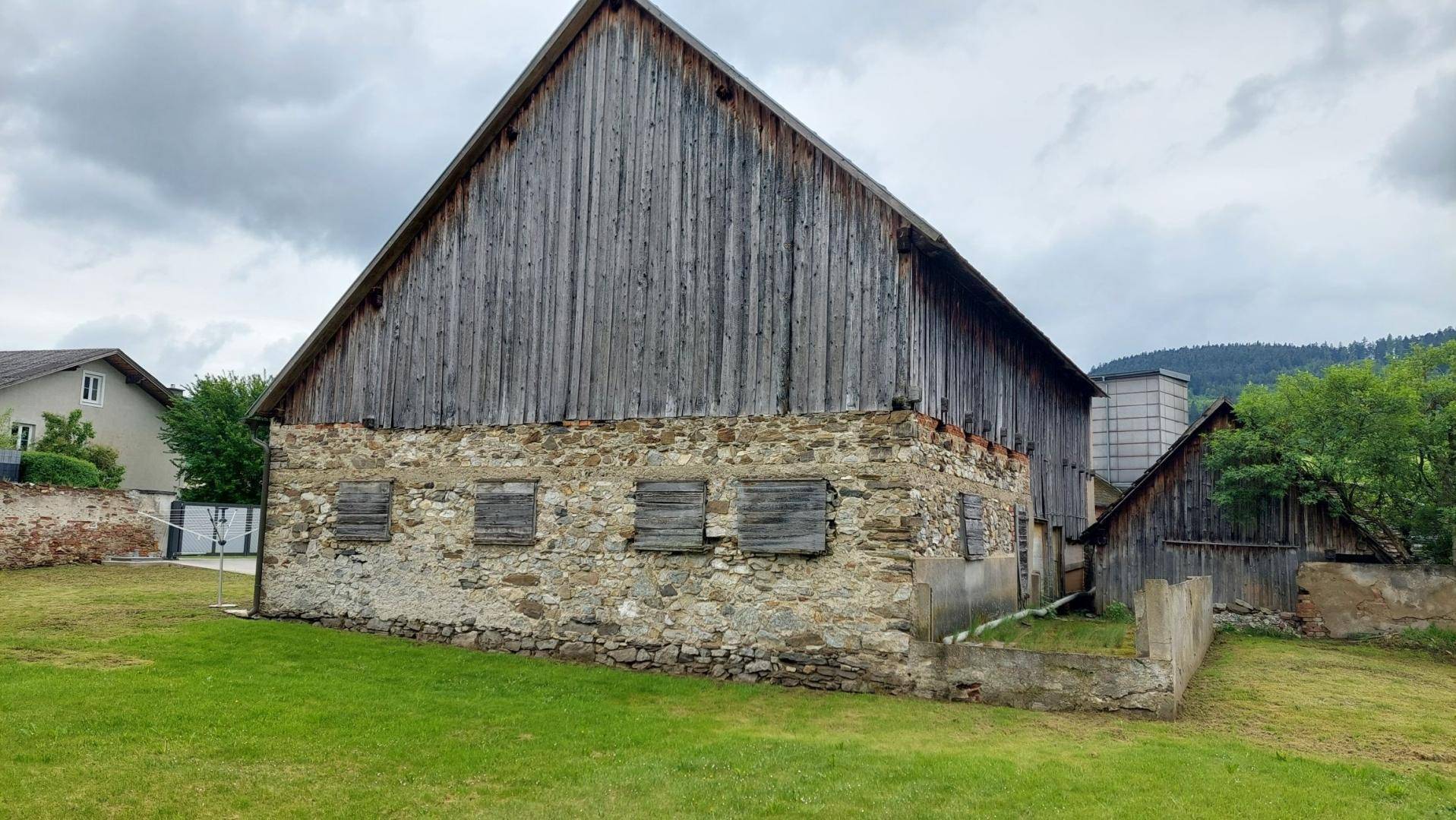 Die imposante Holzscheune mit Steinfundament und traditionellem Satteldach, eingebettet in grüne Landschaft.