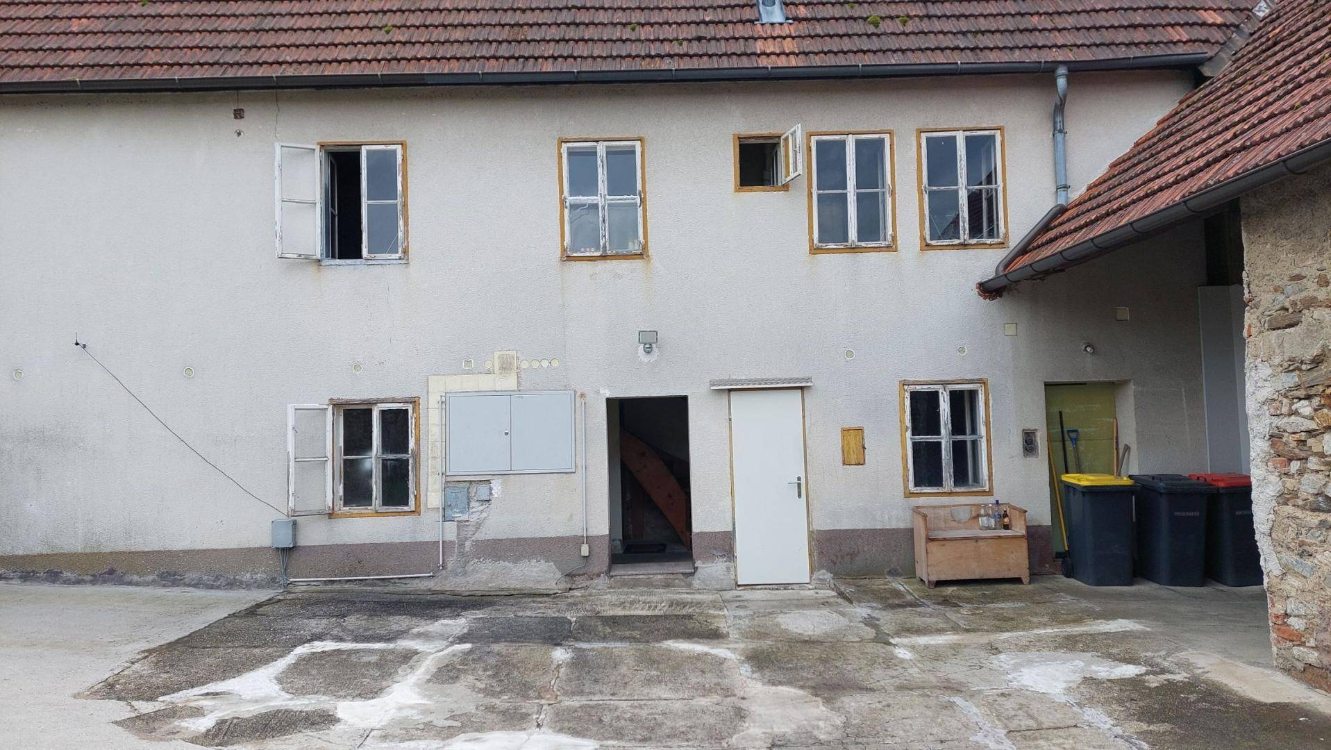 Fassade des Wohnhauses mit mehreren Fenstern und Zugang zum gepflasterten Hofbereich, in gutem Zustand.
