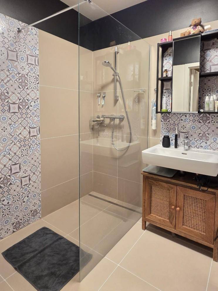 Ebenerdige Dusche und Waschbecken mit dekorativen Fliesen im modernen Badezimmer.