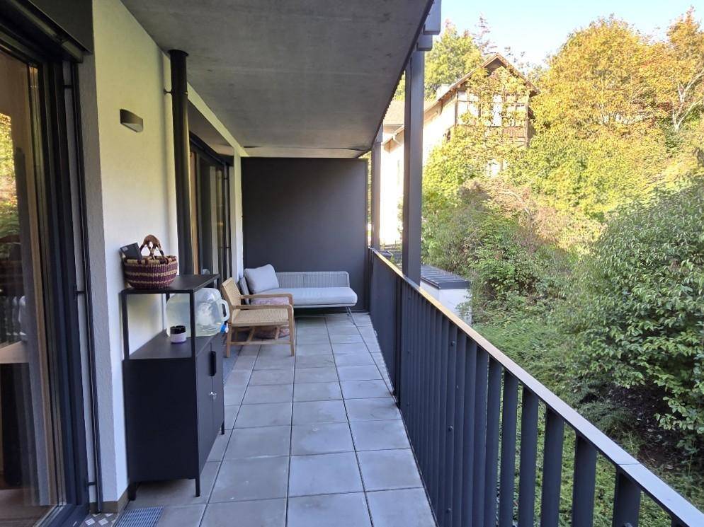 Langer Balkon mit Fliesenboden, Sitzgelegenheiten und Blick ins Grüne.