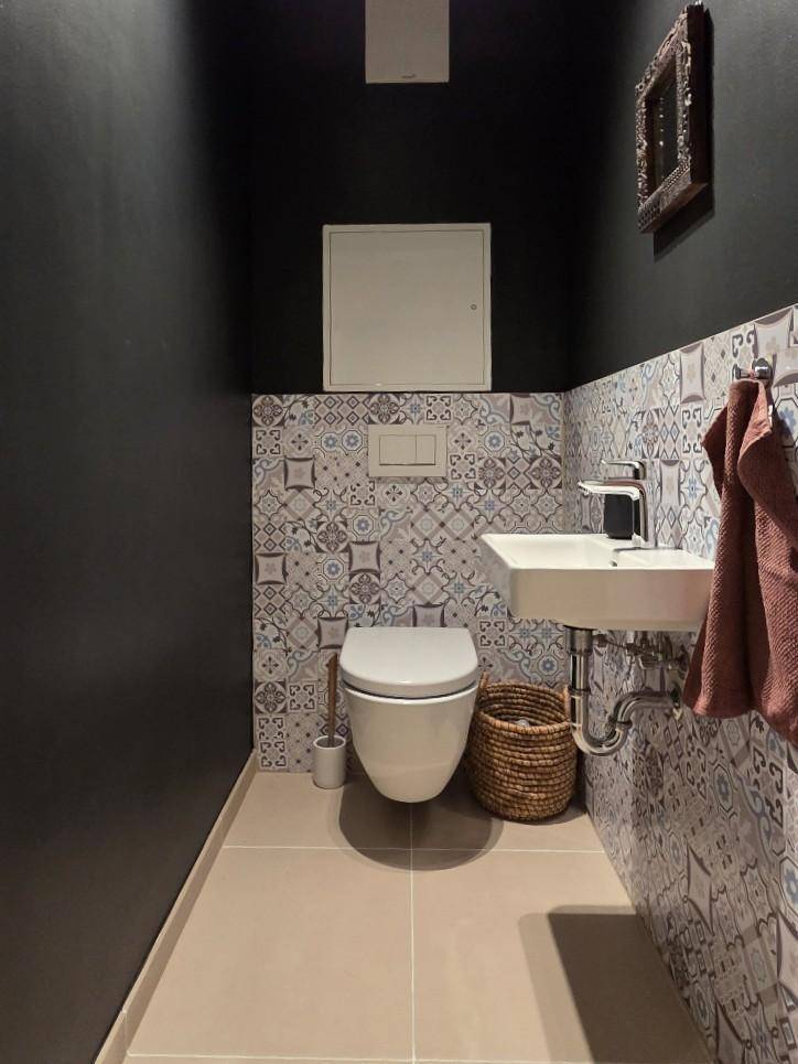 Gäste-WC mit Wand-WC, kleinem Waschbecken und dekorativen Fliesen an der Wand.