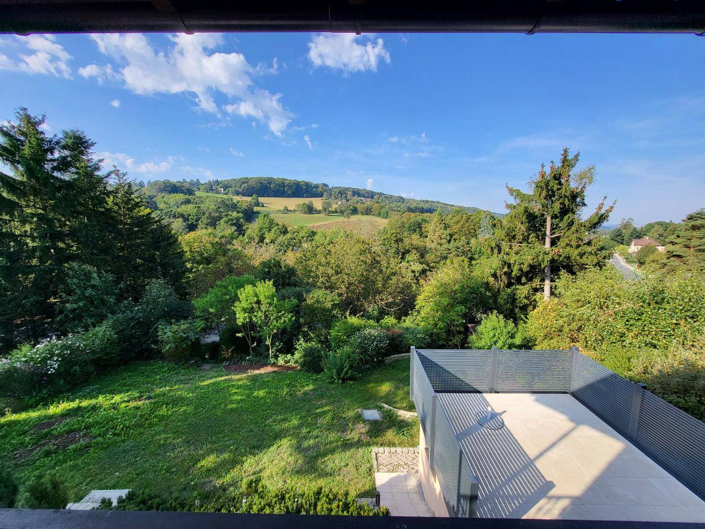 Weitläufiger Blick von der Terrasse auf die grüne Hügellandschaft und den Wald.