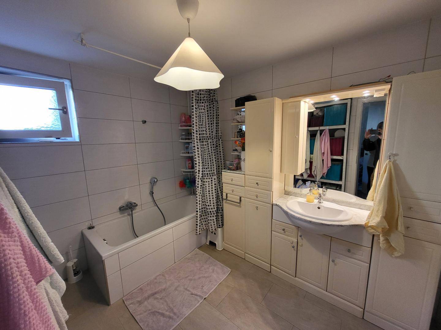 Gefliestes Badezimmer mit Badewanne, Waschbeckenunterschrank und Spiegelschrank.