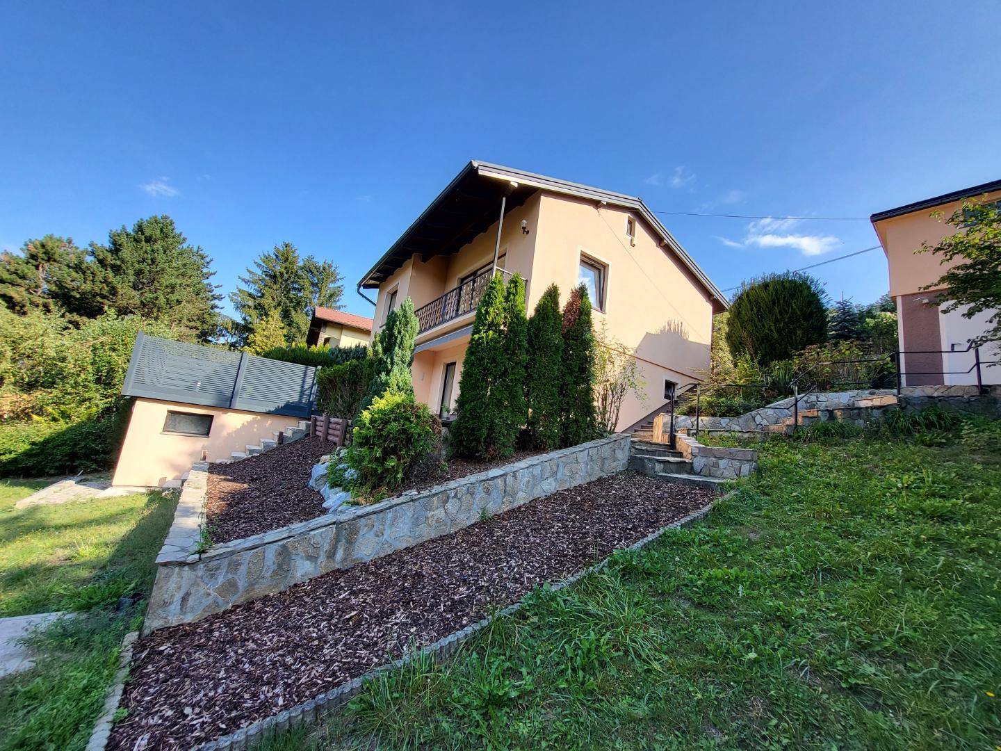 Seitenansicht des Hauses mit terrassiertem Gartenbereich und üppiger Bepflanzung.
