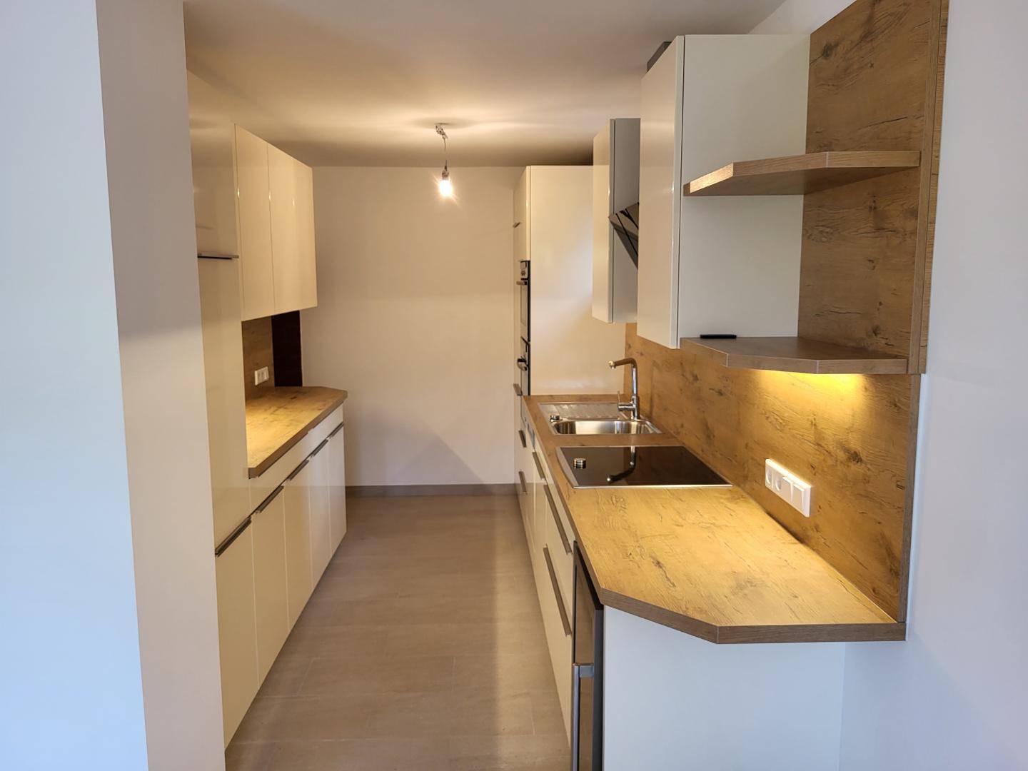 Moderne Küche mit weißen Hochglanzfronten, Holzoptik-Arbeitsplatten und integrierten Geräten.
