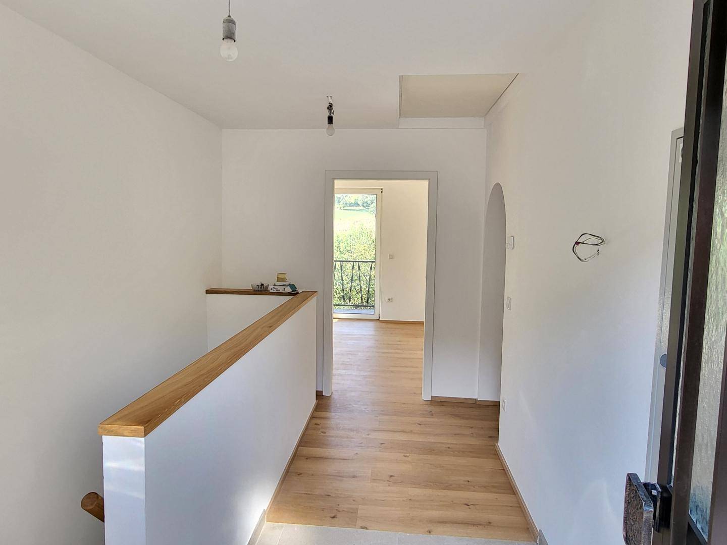 Heller Flur mit Laminatboden und Holzgeländer, der zu weiteren Räumen führt.