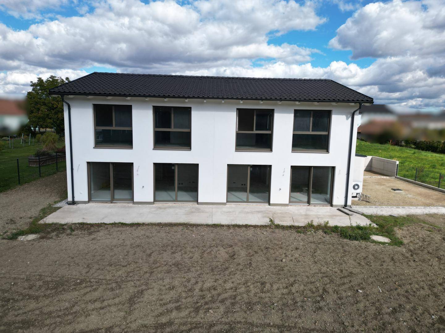 Rückansicht eines modernen Neubaus mit großen Fenstern und Schiebetüren zum zukünftigen Gartenbereich.