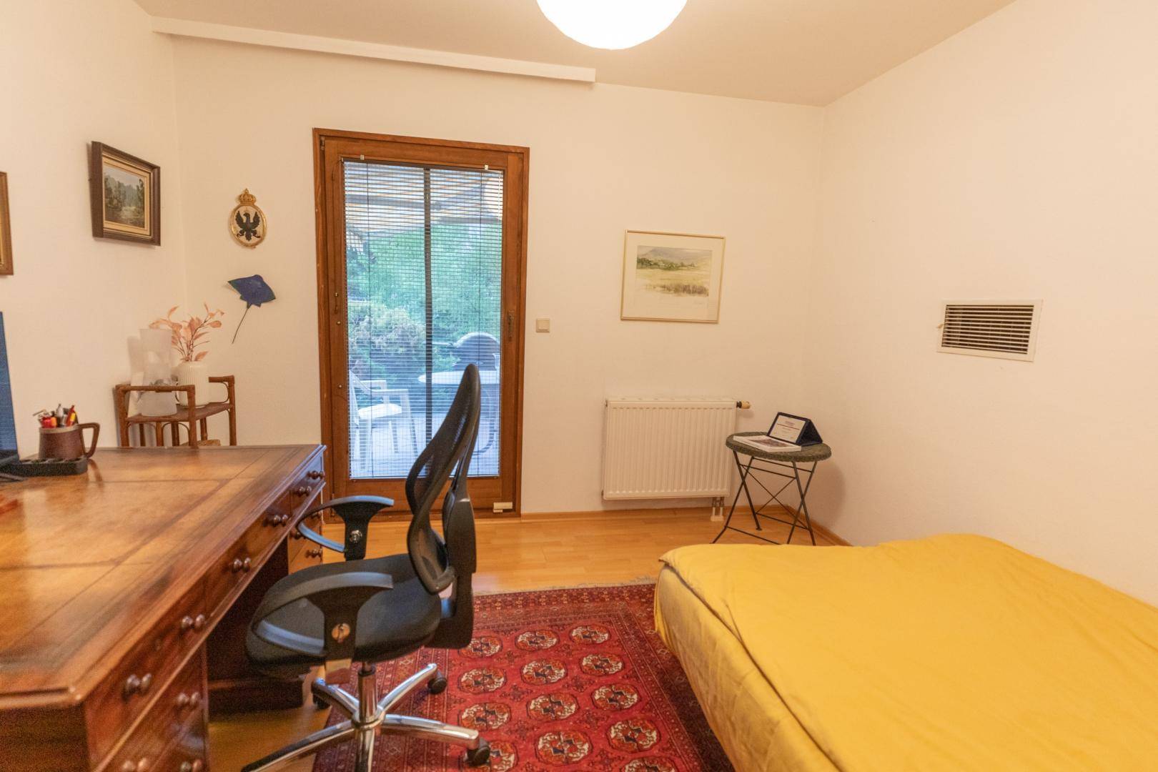 Schlafzimmer mit Arbeitsbereich, Parkettboden und Zugang zu einem Außenbereich.