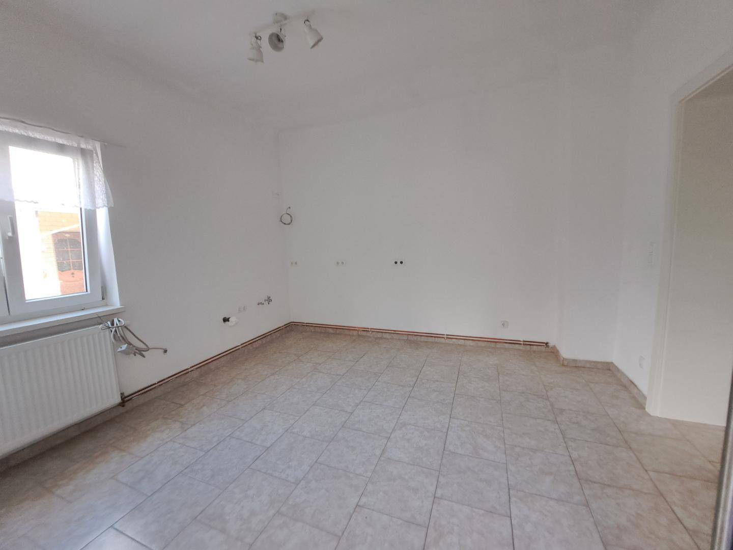 Leerer Raum mit Fliesenboden, Heizkörper und Fenster, bereit für die Einrichtung.