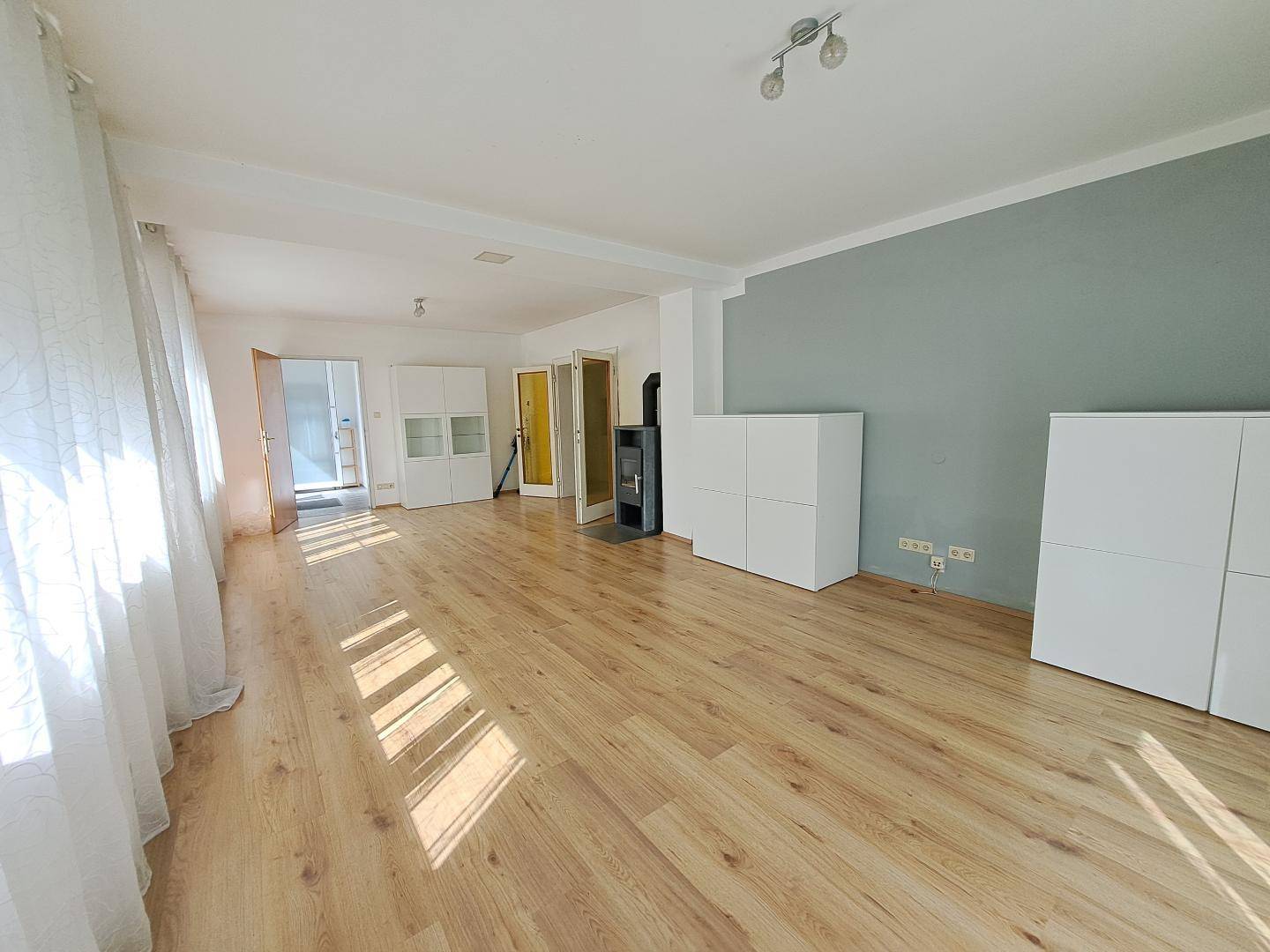 Geräumiges Wohnzimmer mit hellem Laminatboden, Kaminofen und viel Tageslicht.