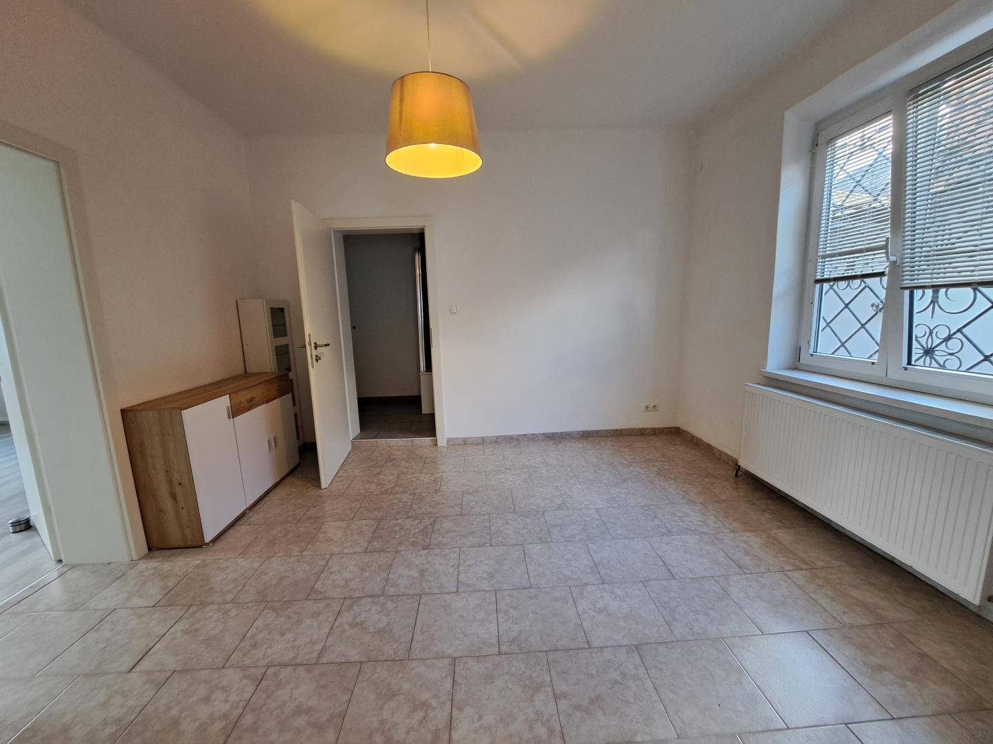 Heller Raum mit Fliesenboden, Fenster und einfacher Deckenleuchte.