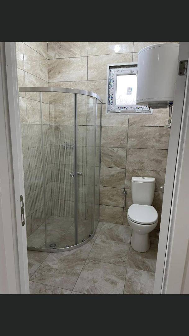 Modernes Badezimmer mit gebogener Glasdusche, WC und Fenster, komplett gefliest.