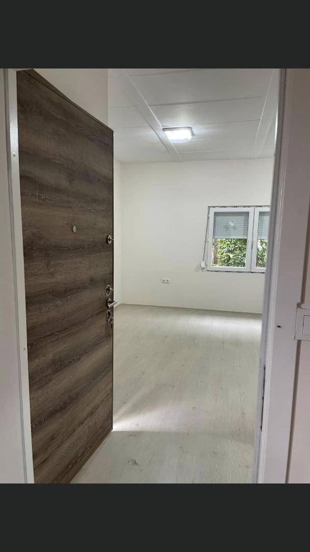 Blick durch eine moderne Holztür in einen leeren Raum mit hellem Laminatboden und Fenster.