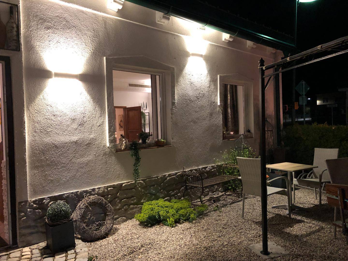 Abendliche Ansicht einer Hauswand mit Außenbeleuchtung und einem kleinen, bekiesten Terrassenbereich.