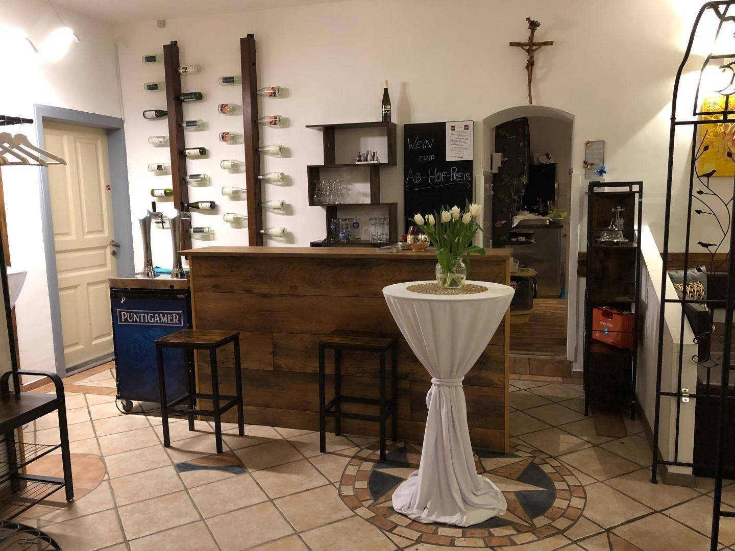 Innenbereich mit einer Holztheke, Fliesenboden und Weinregalen, dekoriert mit frischen Blumen.