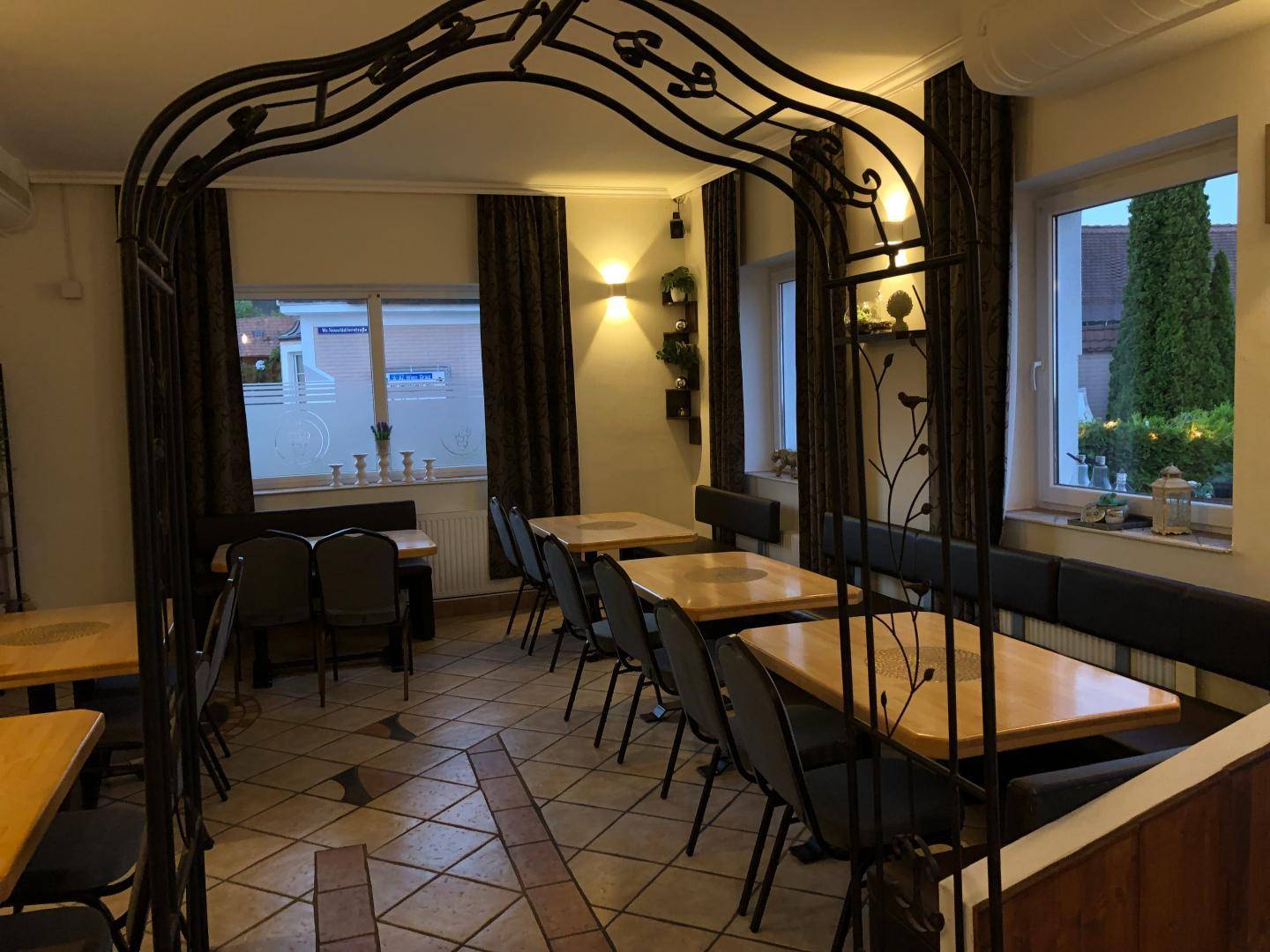 Gemütlicher Speisesaal mit Holztischen, gepolsterten Bänken und dekorativen Metallbögen.