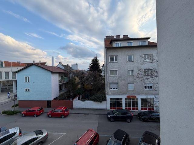 Weitläufiger Blick vom Balkon über die Straße mit verschiedenen Gebäuden und Bäumen.