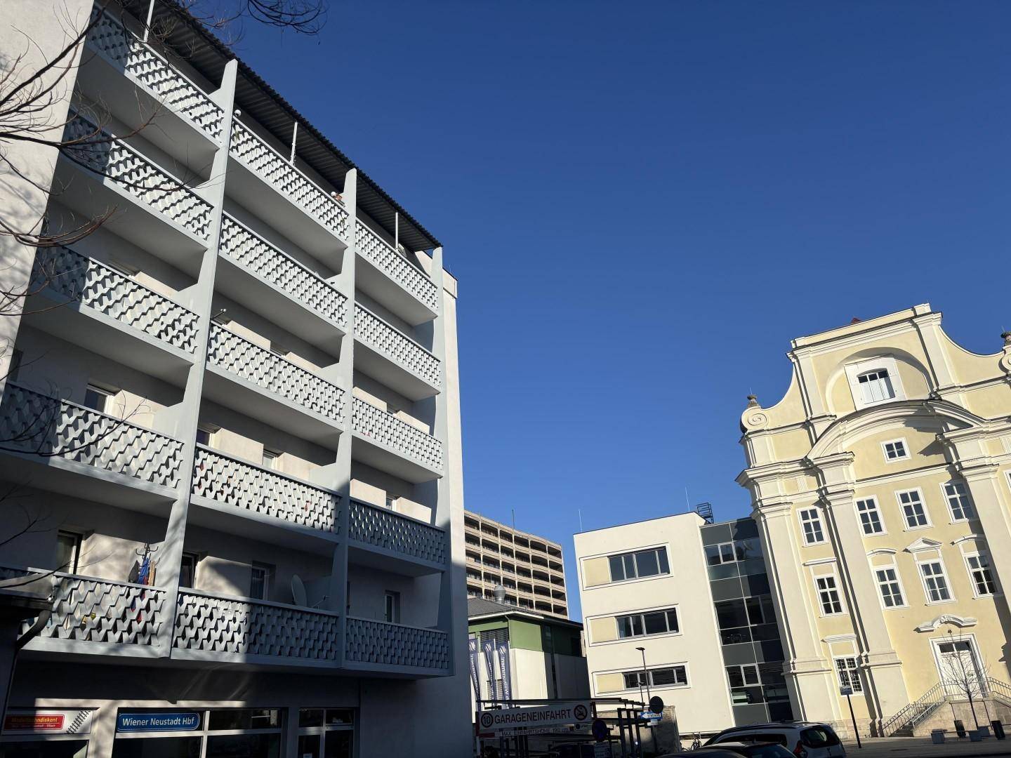 Ansicht eines modernen Mehrfamilienhauses mit Balkonen unter strahlend blauem Himmel.