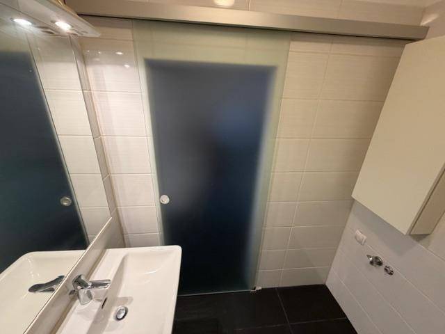 Badezimmer mit Waschbecken, Spiegel und Schiebetür aus Milchglas.