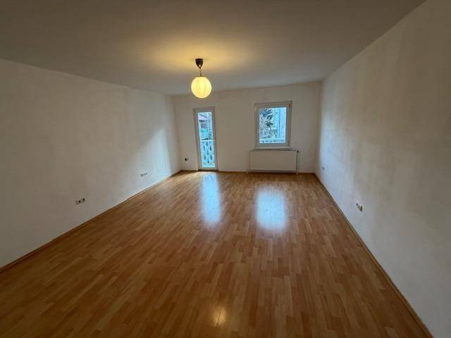 Geräumiger, heller Raum mit Laminatboden und Zugang zu einem kleinen Balkon.